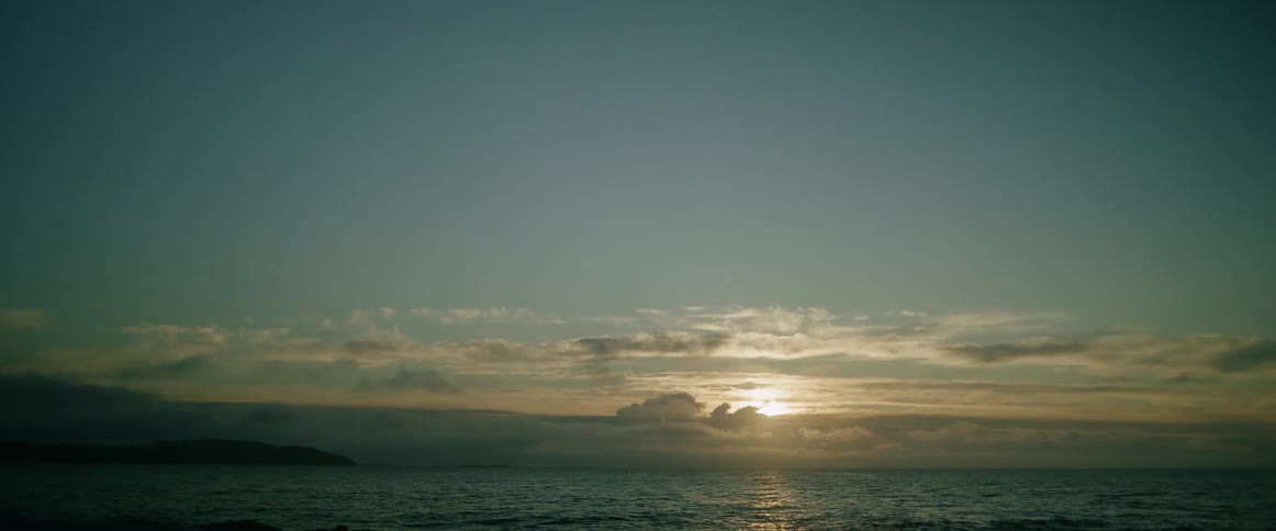 Sun partially covered by clouds over the ocean outdoors during dusk or dawn