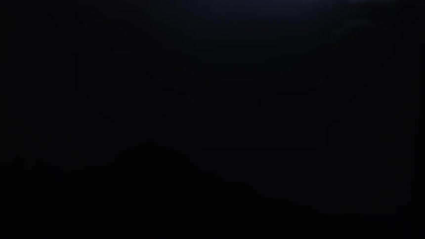 Intense lightning bolts streak across night sky above mountain silhouette