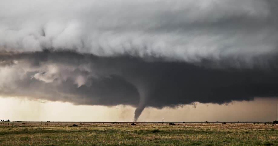 Dark cloud fills the sky as a tornado spins across rural land
