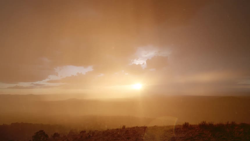 The sun sets over mountains as snow falls from the sky