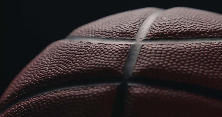 A closeup macro shot shows a dark orange basketball slowly rotating against a black background