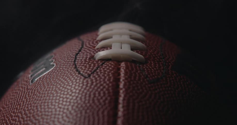 The camera is close up on the football to where you can only see the area around the laces and it is steaming