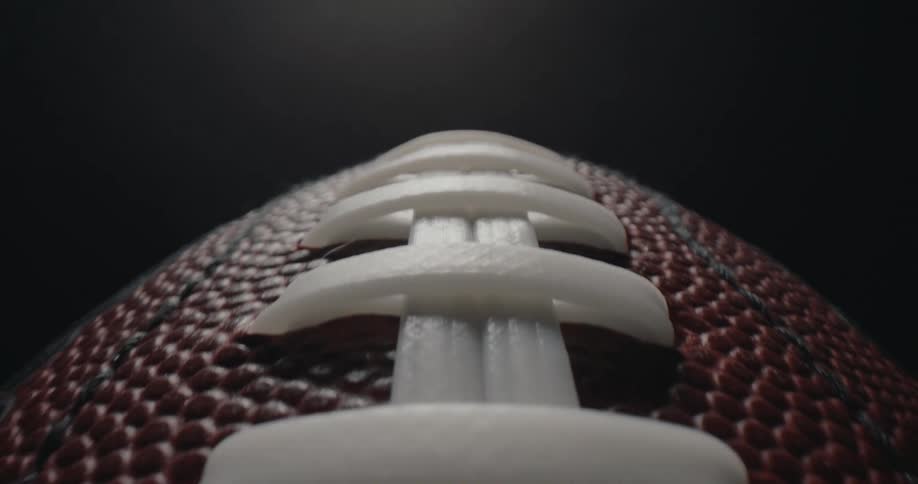 Central stitching of an american football in closeup against a dark background