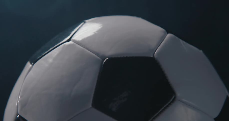 A closeup shot shows a classic black and white soccer ball rotating slowly against a dark smoky background
