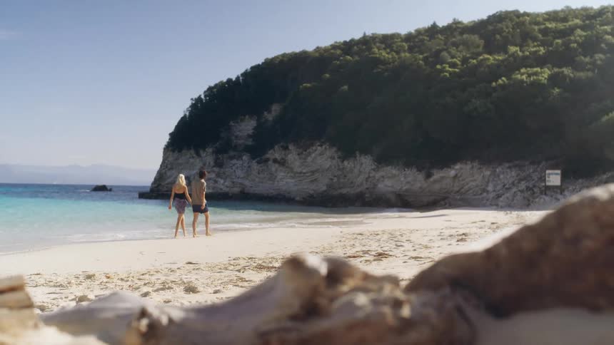 A man and woman walk along a sunny beach together