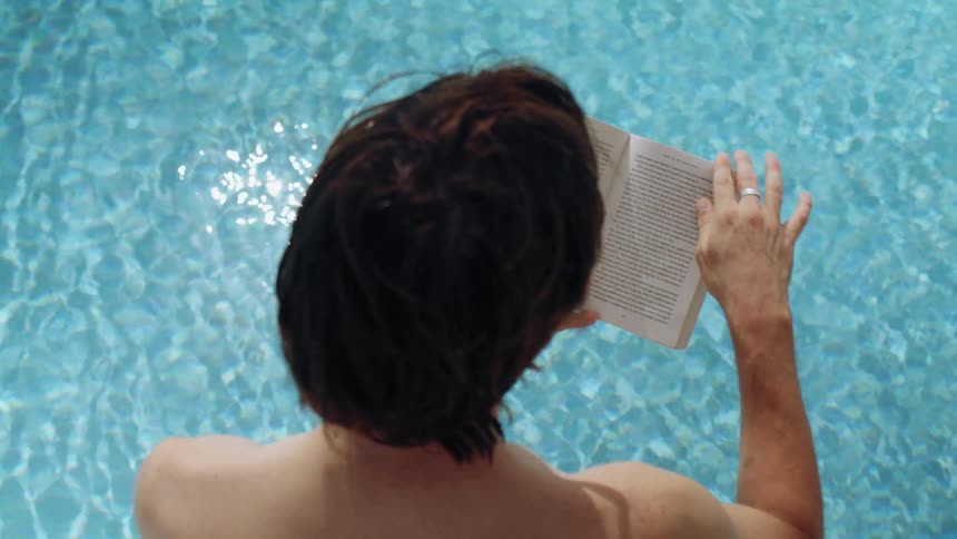 Person reads book while relaxing in clear pool