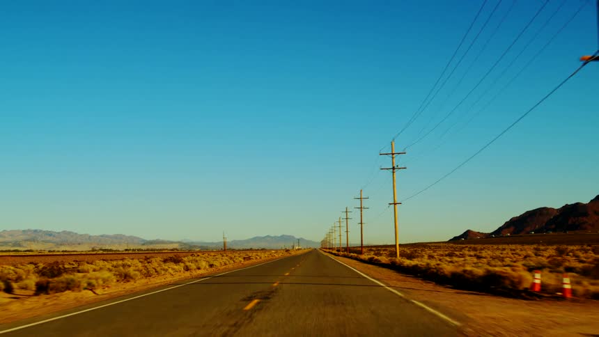 Straight road crossing a desert landscape with aligned power poles under a clear blue sky