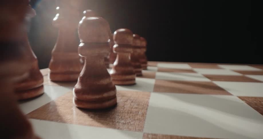 A lowangle cinematic shot moves past a row of wooden chess pawns lined up on a checkered board highlighted by a warm light source creating a strong lens flare against a dark background