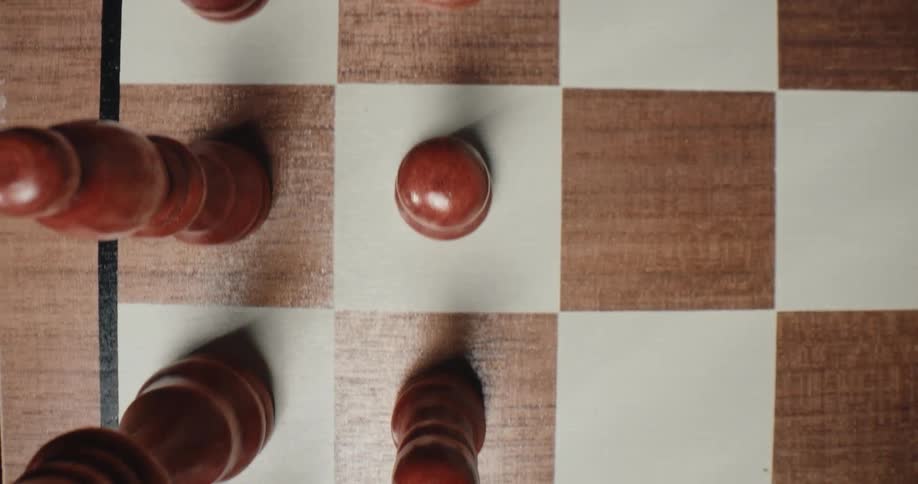 A topdown tracking shot moves across a wooden chessboard passing over brown pawns and a rook positioned on the light and dark squares of the playing surface