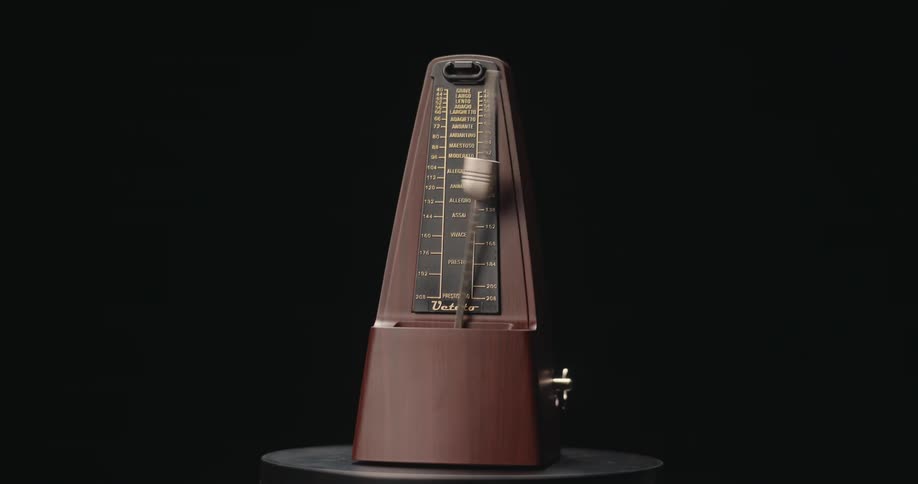 A medium view of a traditional wooden mechanical metronome with a swinging pendulum ticking back and forth against a dark background as the lighting shifts