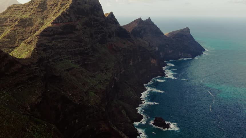 Aerial view of steep volcanic cliffs meeting a turquoise ocean along a rugged coastline