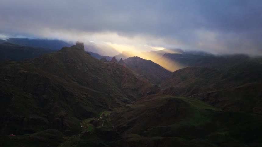 Mountain valley with dark slopes under dense clouds and beams of sunlight breaking through in the distance