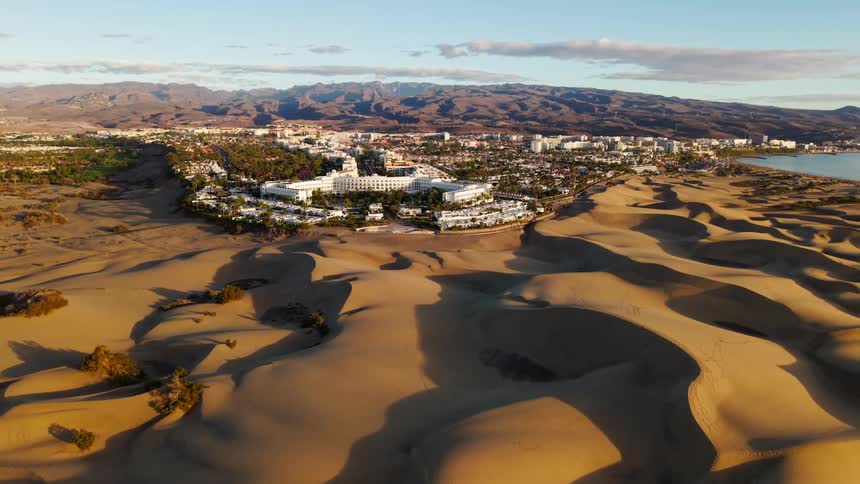 Dunes cast shadows over coastal city between mountains and ocean