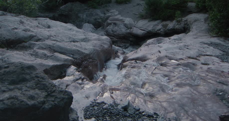 Flowing water crosses rounded rocks in natural terrain with sparse vegetation