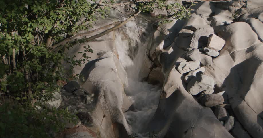 Water cascade flows through a crevice in lightcolored rocks surrounded by vegetation