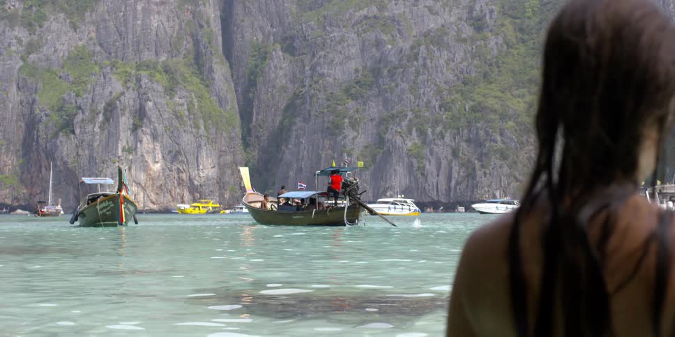 A woman walks on a beach with several boats in the water