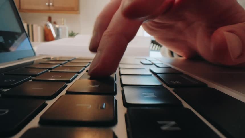 A person types on a laptop keyboard at midday bright natural light illuminating their hands as they work