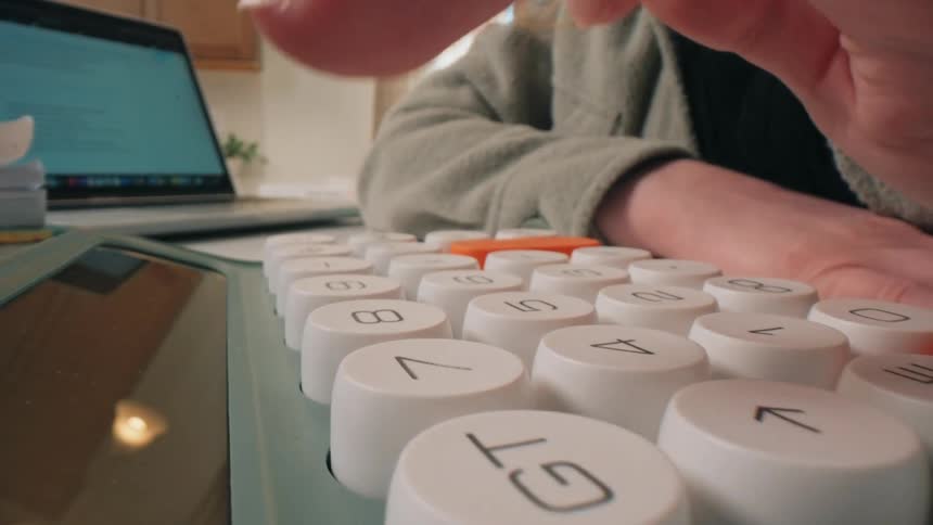 Human hands keying an operating machine on a desk next to a laptop computer indoors during day time