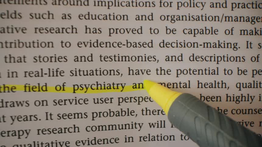 Printed text passage with a sentence highlighted in yellow being pointed at by a marker