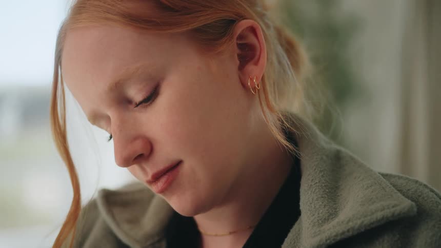 Redhaired person with calm expression looks downward in soft light