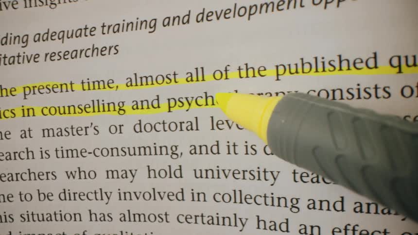 A person using a yellow marker to highlight a sentence in a publication