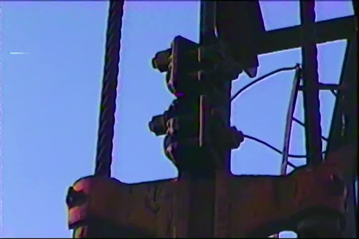 There are two thick textured cables running vertically on either side of the central mechanism these lines remain parallel to each other and serve as the guide or support for the moving machinery against the clear blue sky