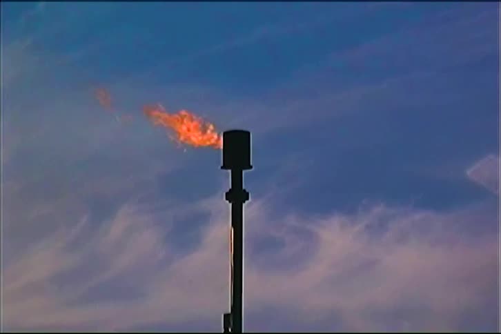 Bright orange flame from flare stack against blue sky with wispy clouds
