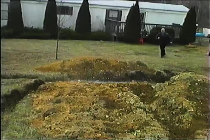 Remotecontrolled car speeds across a yard and jumps over a dirt mound into a puddle of water a man standing nearby then runs over to the spot where the car landed