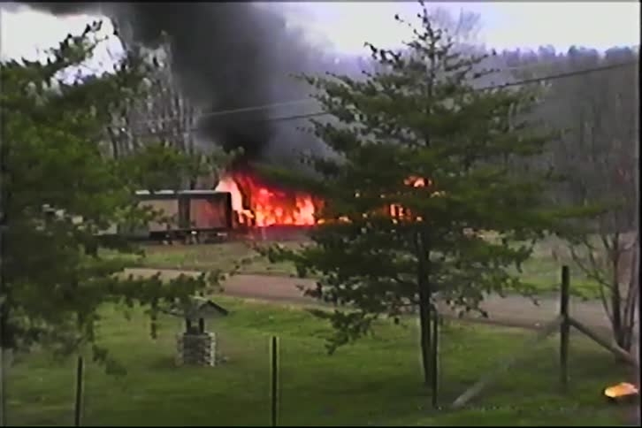 Intense fire engulfs house in rural area with thick smoke rising into the sky