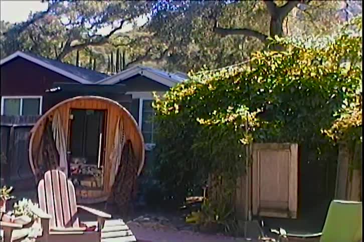 The backyard of a suburban home surrounded by trees with wooden chairs spread across the yard on a sunny day