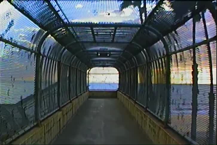 Fenced walkway reveals sky and landscape beyond lit by gentle evening light