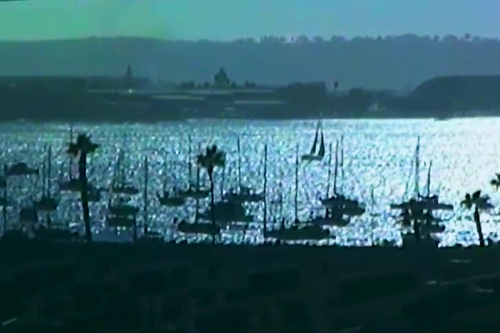 A coastal harbor with sailing boats and cargo ships at sunset