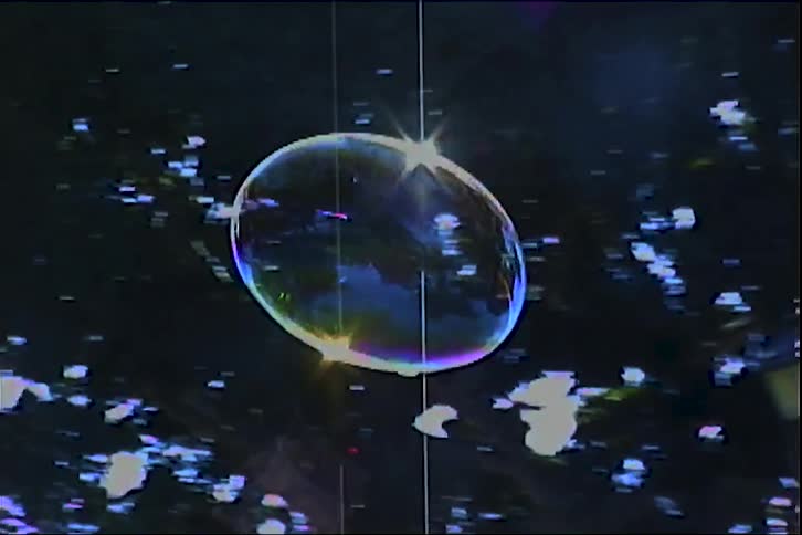 Soap bubble floating outdoors with trees and buildings in the background