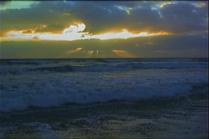 Golden sun breaks through clouds over churning sea at dawn
