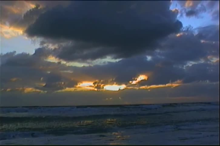 Golden light piercing dense clouds over ocean at dawn