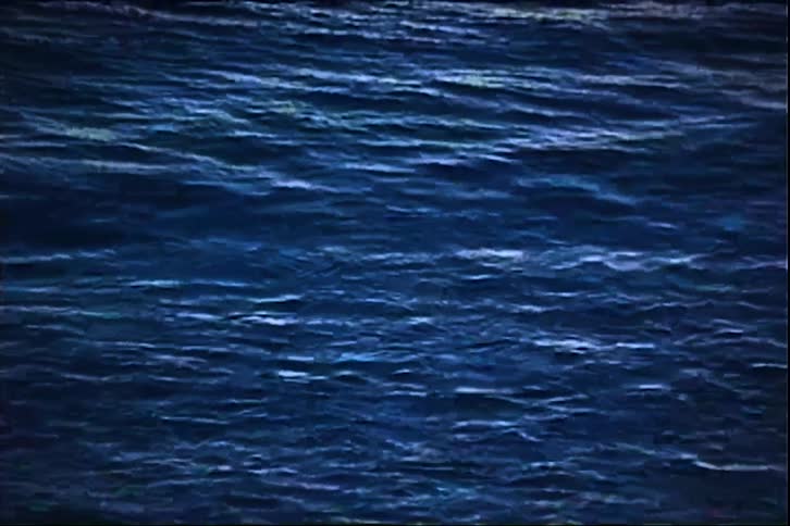 An ocean stretches toward the horizon at sunset with a series of small waves forming gently across the glowing warmlit surface
