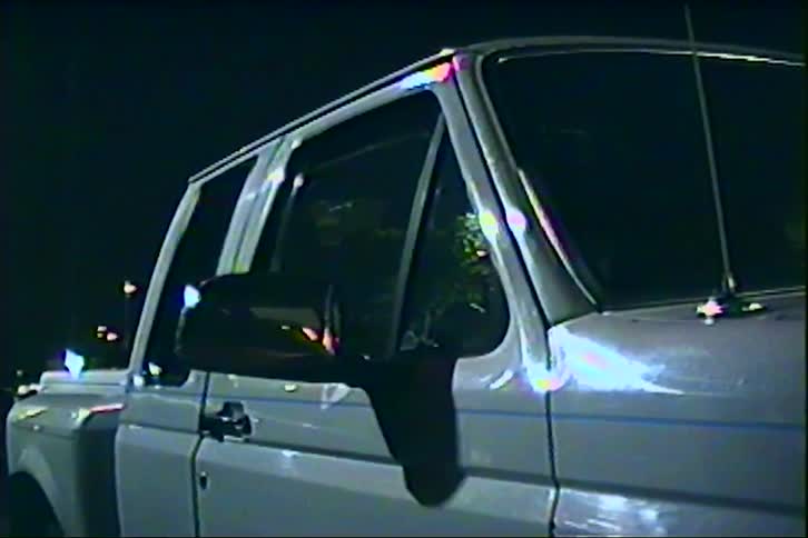 A white pickup truck is parked at night with city lights reflecting off its windows and body