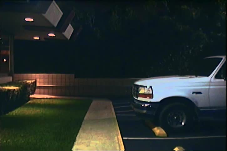 Nighttime parking lot with a white pickup truck near a lit building entrance