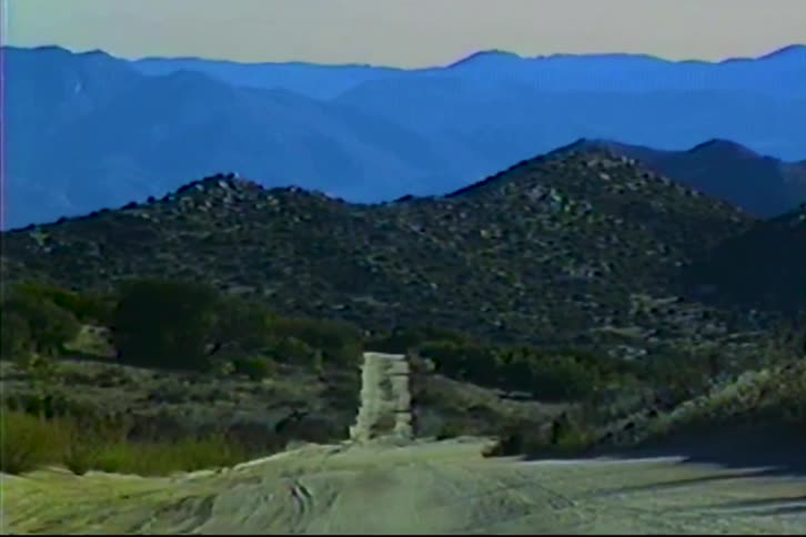 Dirt road leading to an isolated stone structure in a mountainous landscape