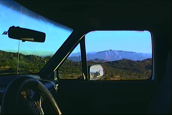 Vehicle interior with steering wheel in the foreground and desert landscape visible through the side window and windshield