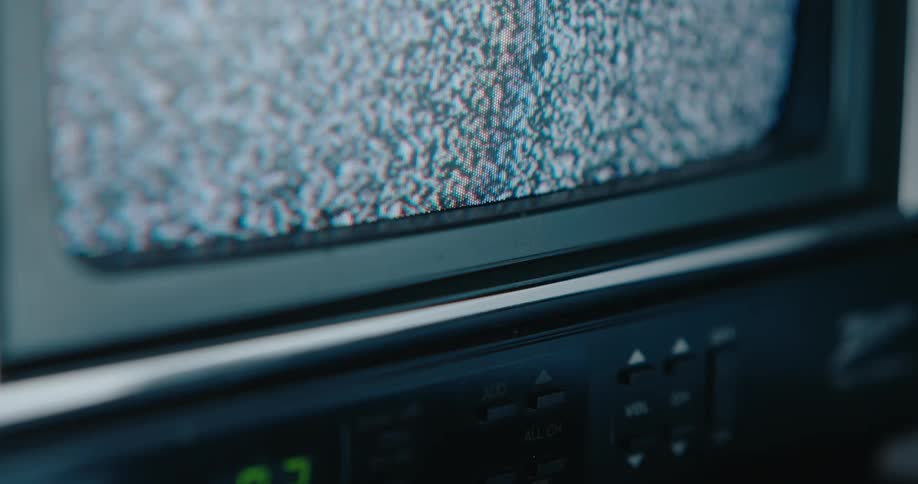 In a closeup angled shot the flickering static of an old crt television screen fills the frame sitting atop a vintage vcr