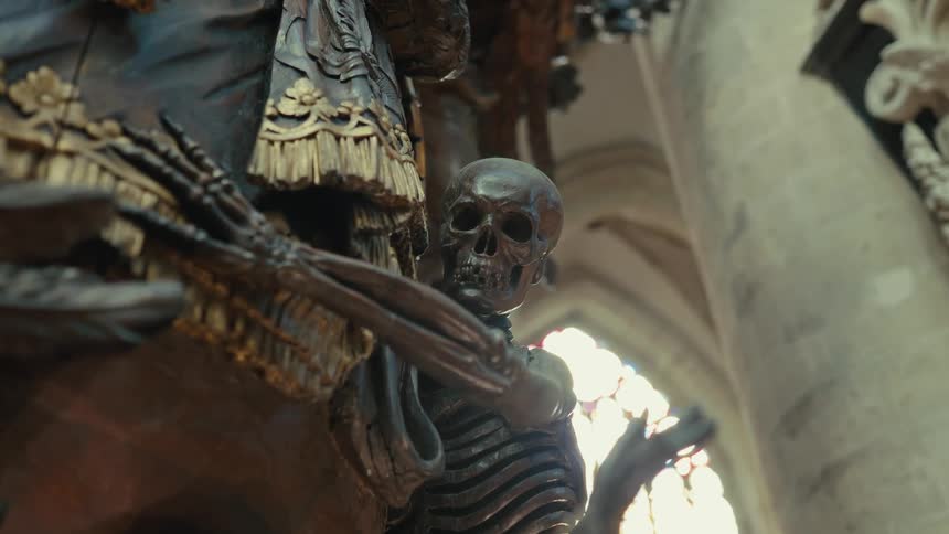 Skeleton sculpture in a religious setting with baroque ornamental elements in the background