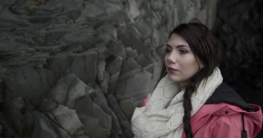 A woman walks tracing her hand on rocks