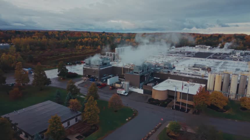Aerial view of a industrial factory emitting steam amid autumn trees under a cloudy sky