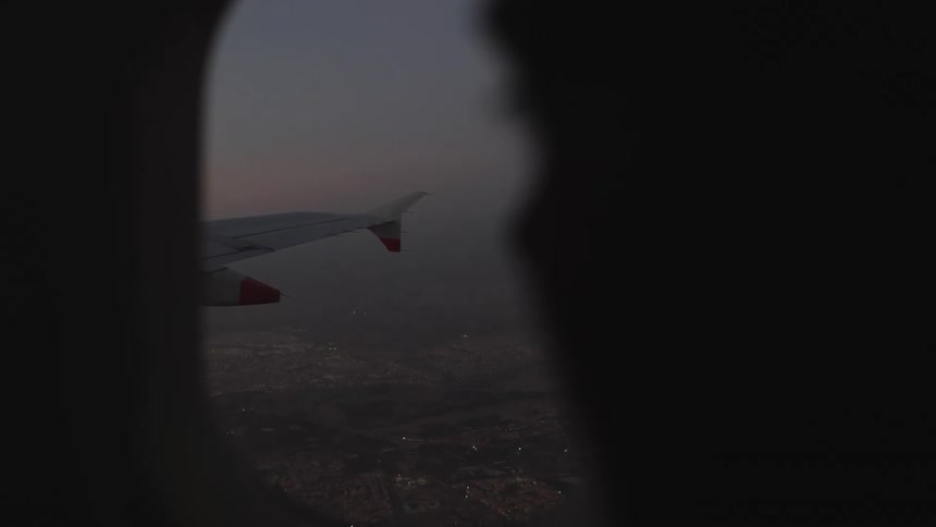Airplane wing seen through a window with a blurred urban landscape under dusk light