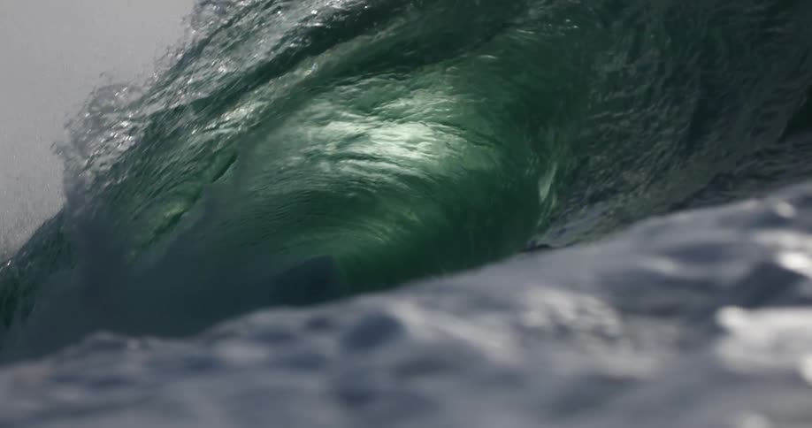 A powerful dark green ocean wave curls over to form a hollow barrel before collapsing into white foam and spray under bright sunlight