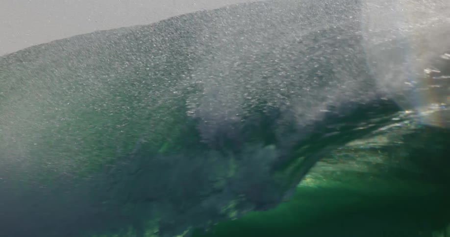 Sunlight shines on a wave splashing as it curls and rolls in to shore