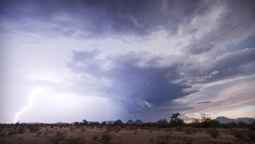 A dramatic storm cloud forms over a flat desert landscape at dusk