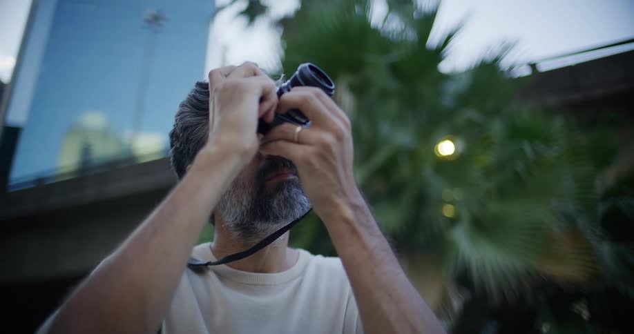Person holds a camera close to the face in an urban setting with greenery in the background