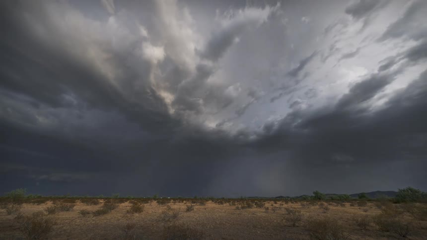 A dramatic timelapse captures a massive thunderstorm brewing over a desert landscape with powerful lightning bolts flashing across the dark swirling sky